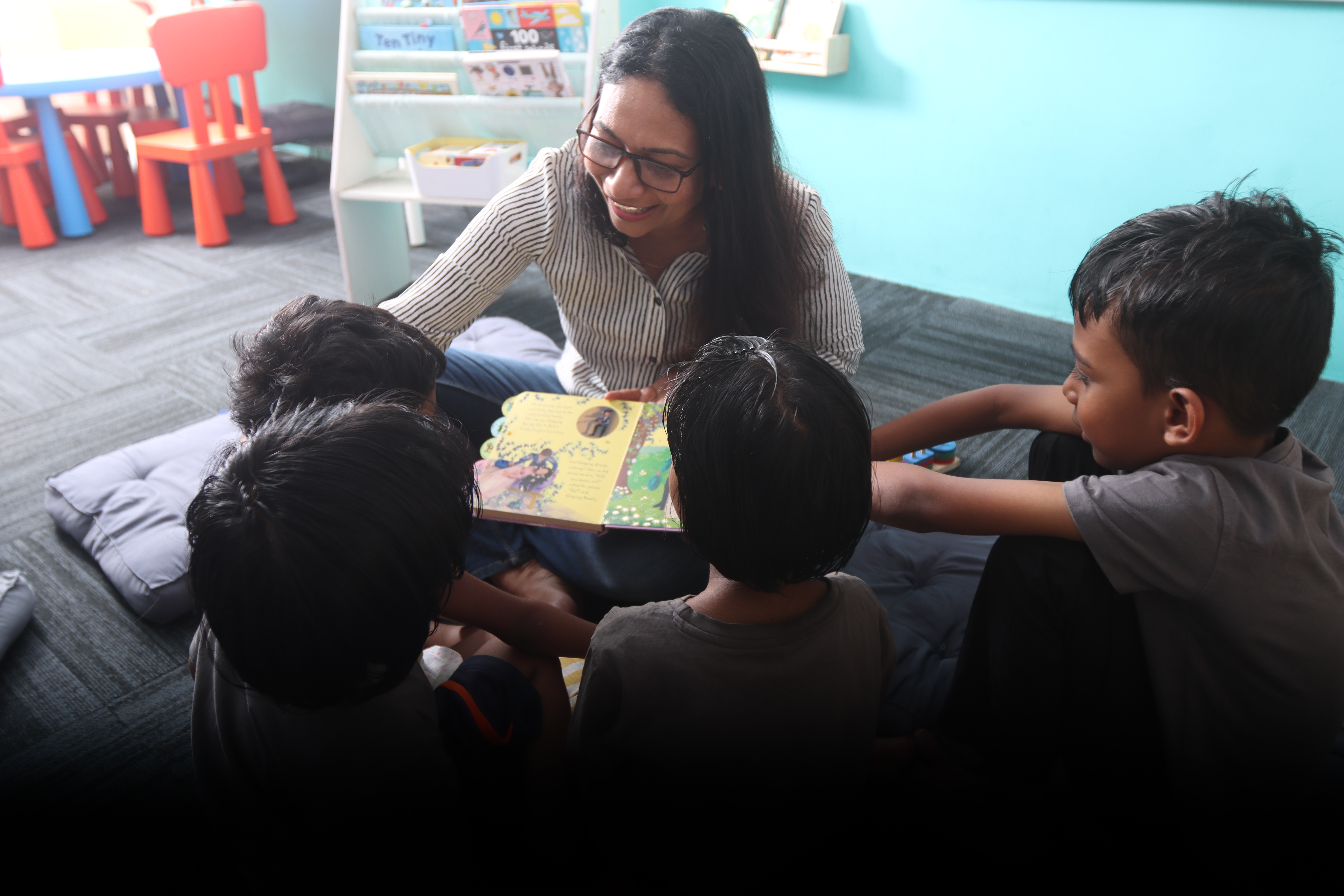 AWS teacher reading a picture book to young children on a floor cushion