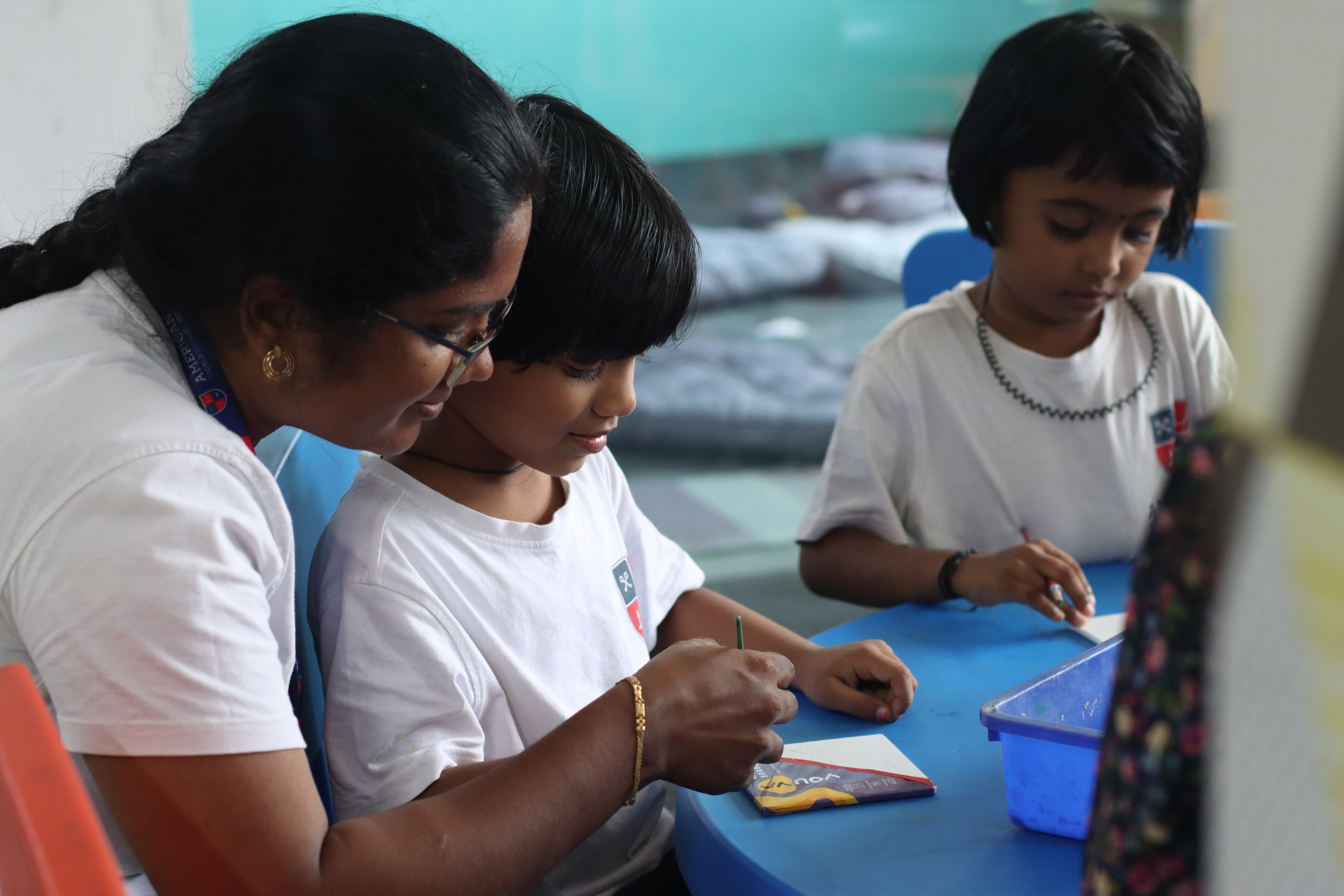 AWS teacher patiently helping two young children draw