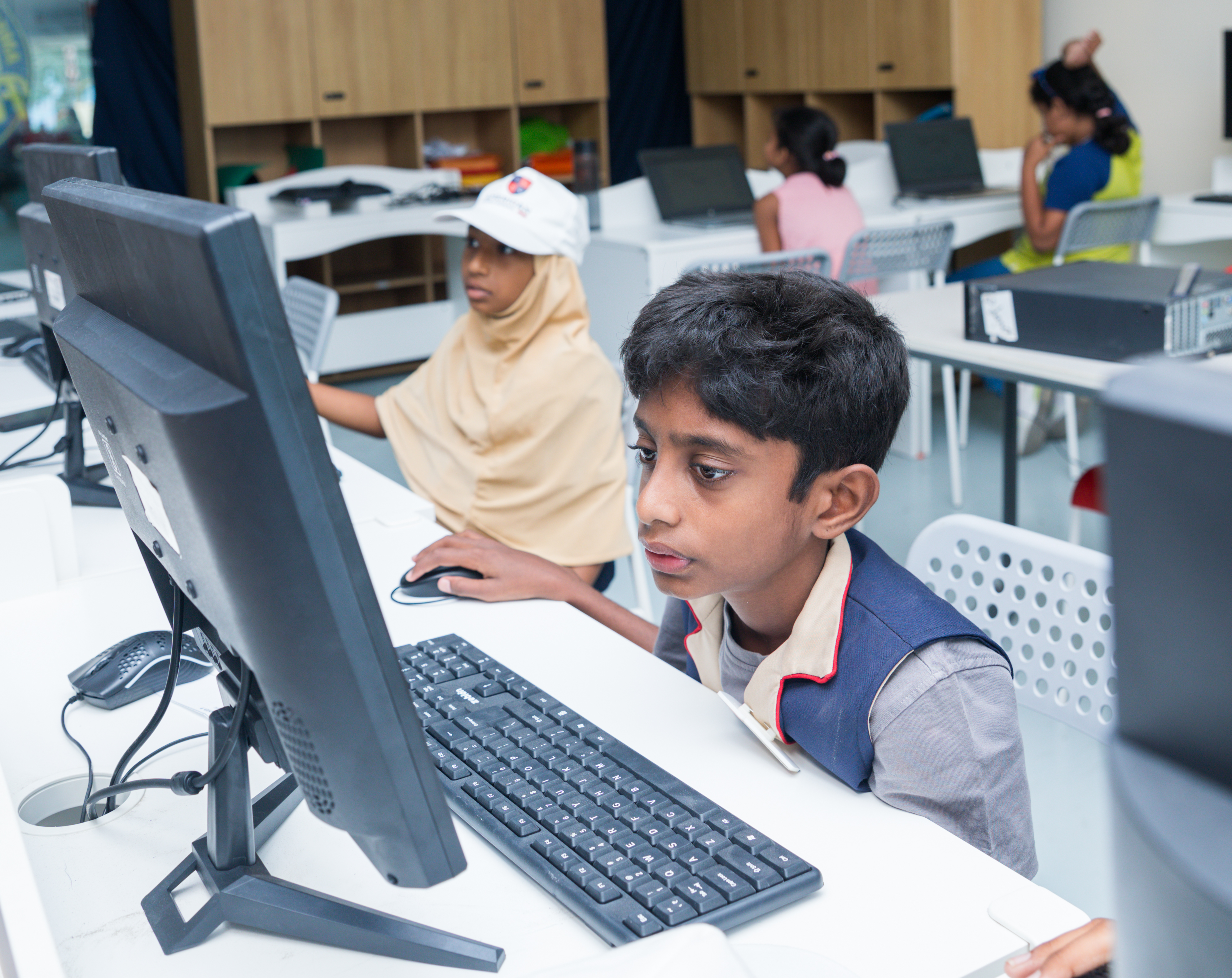A hijabi student and a boy working together at desktop computers in the AWS lab