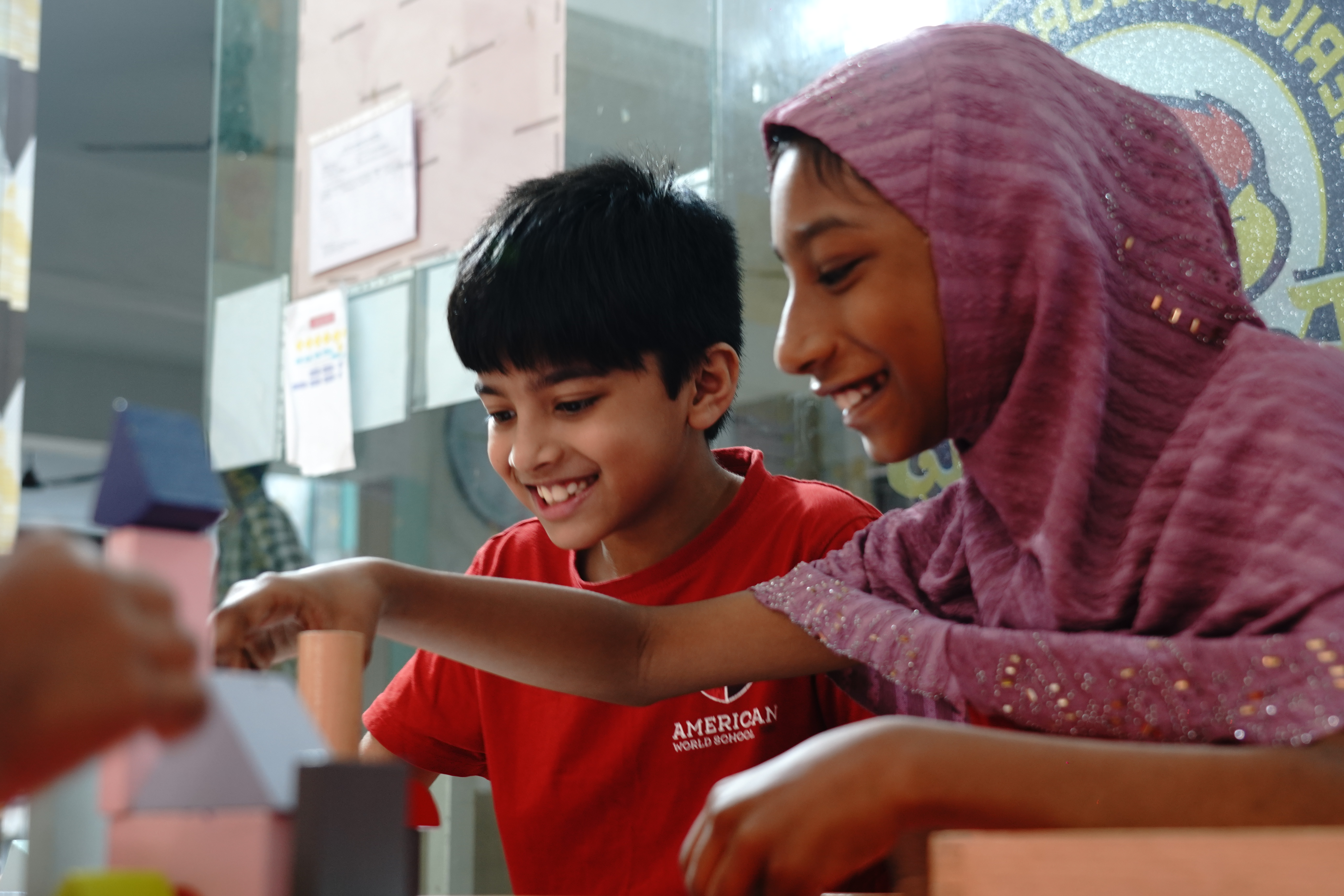 A hijabi girl and a boy laughing while playing with paper craft blocks