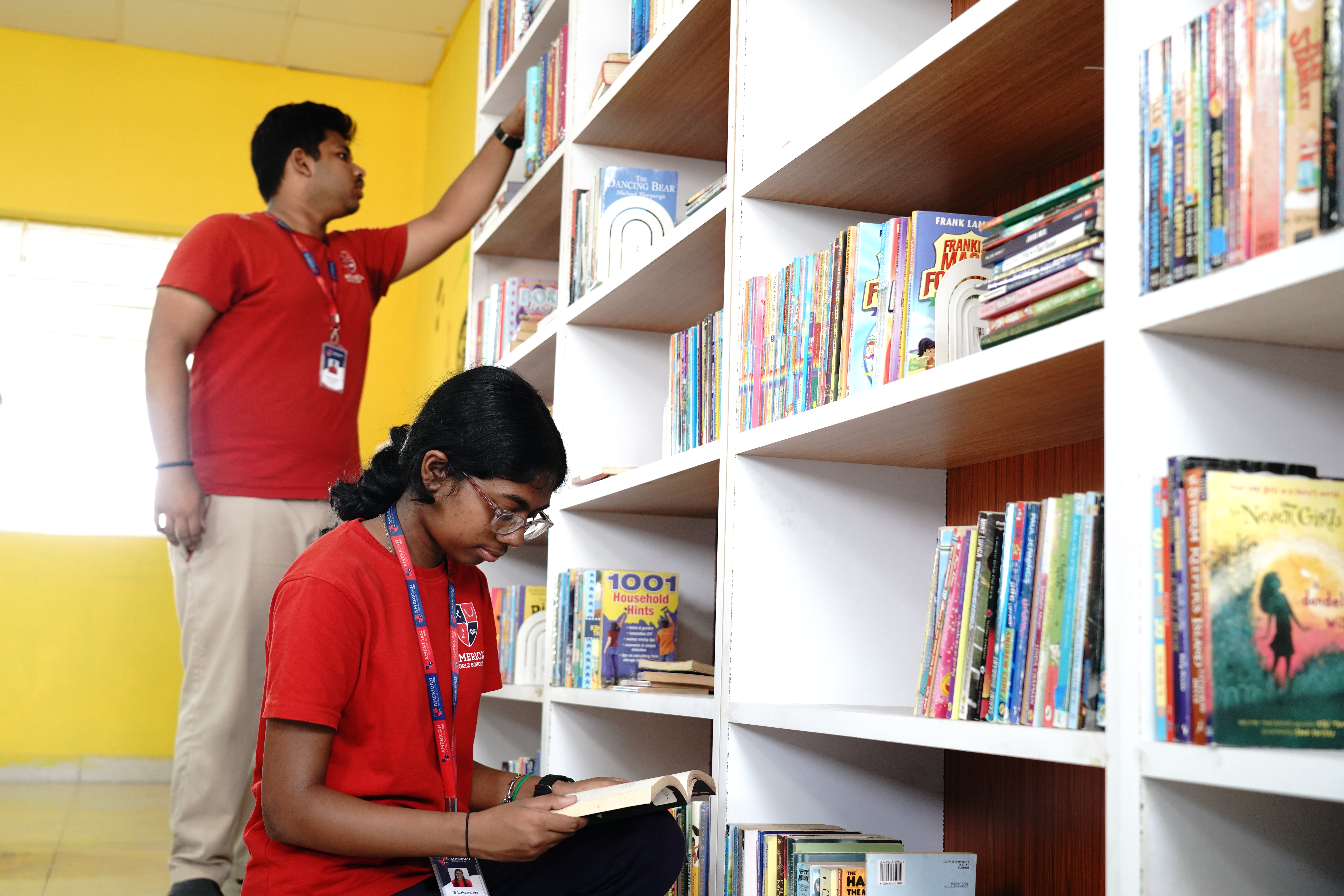Older AWS student helping a younger student find a book on a tall library shelf