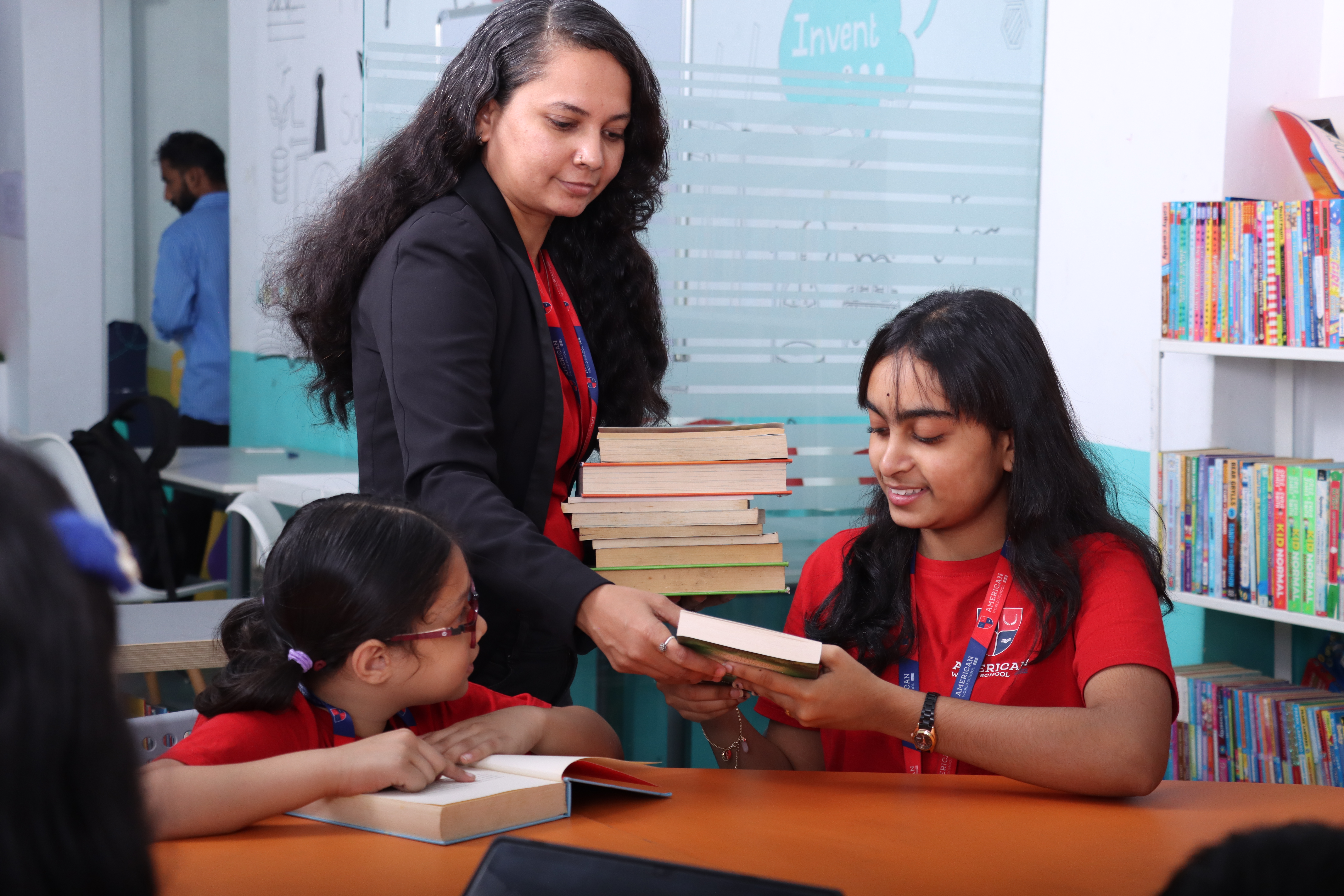 AWS teacher handing books to upper elementary students in the library